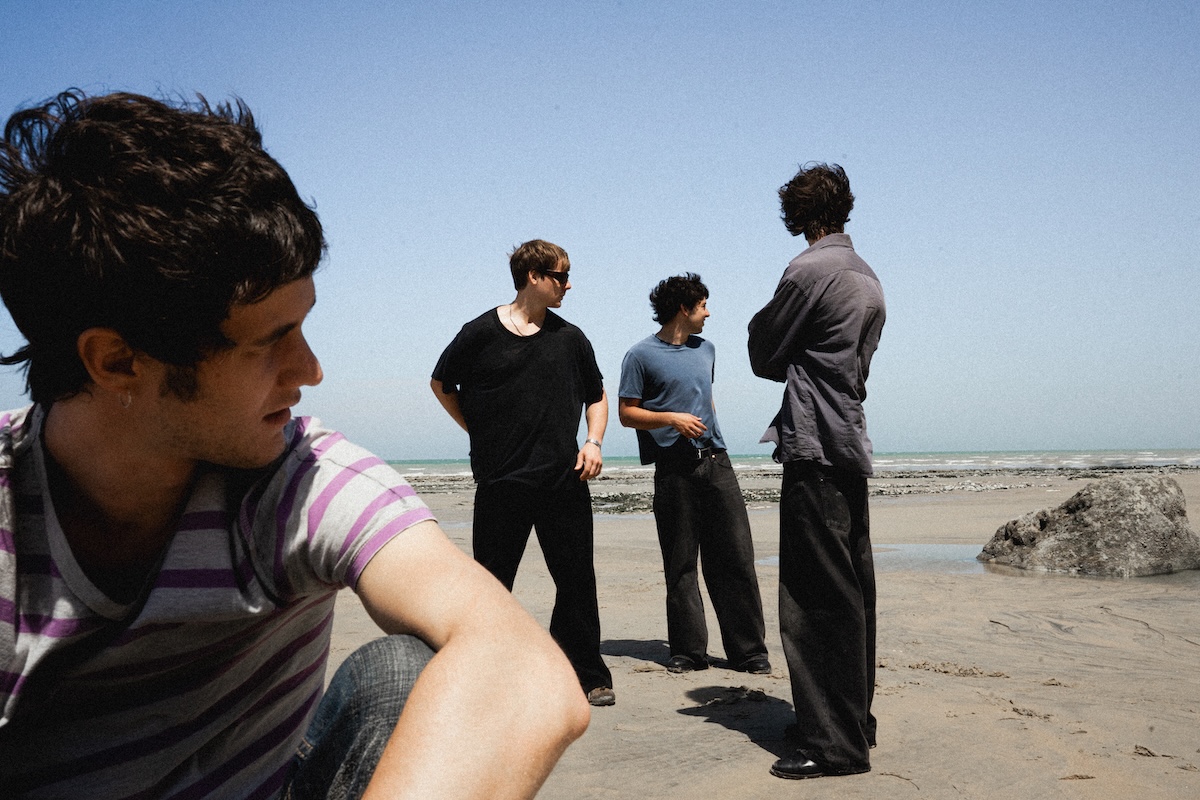 Promotional band photo of Radio Free Alice standing outdoors on a sandy beach under a clear blue sky.